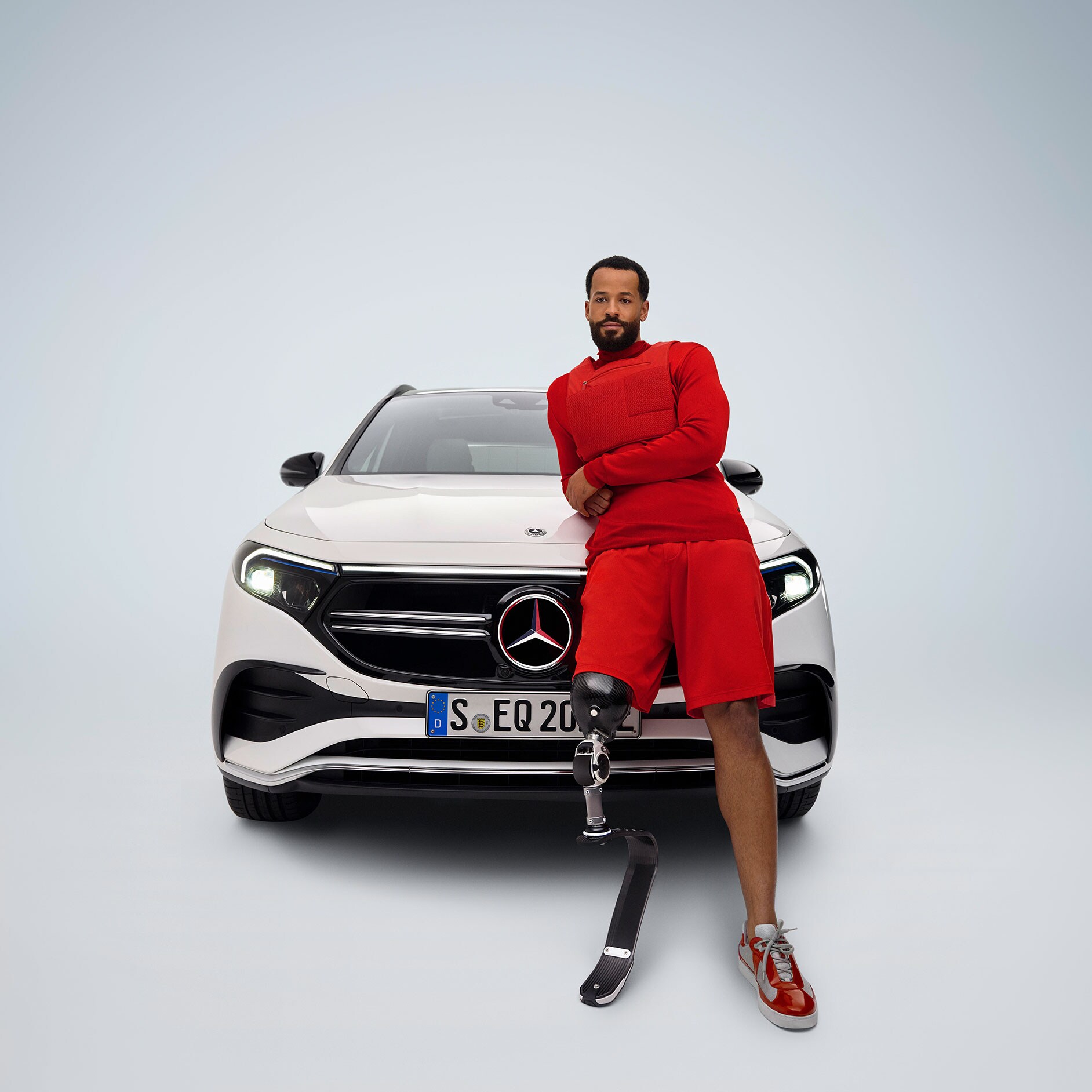 Pedalanpassningar | Körhjälpmedel | Mercedes-Benz En funktionshinderanpassad Mercedes-Benz EQA framifrån, och en man med benprotes.