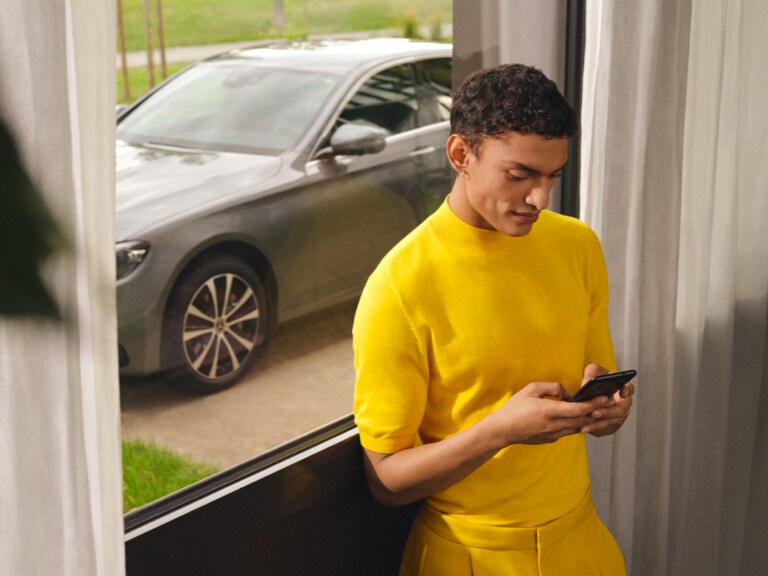 Mercedes-Benz kundtjänst | Mercedes-Benz Finans Person använder sin smartphone inomhus framför sin Mercedes-Benz