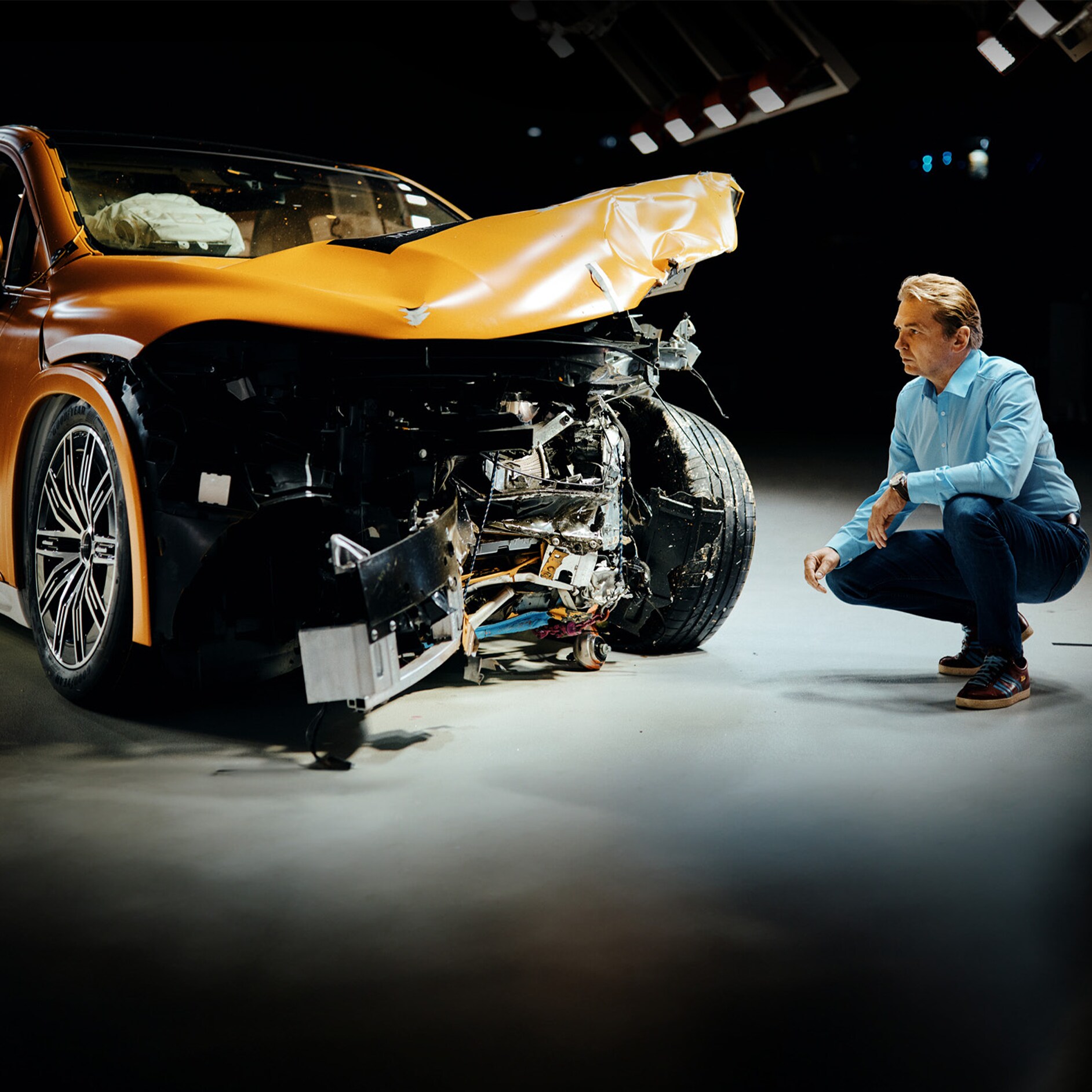 Experter på krocktester | Säkerhet | Mercedes-Benz En krocktestsexpert undersöker en frontalkrockad Mercedes-Benz-bil medan han sitter på huk bredvid den.