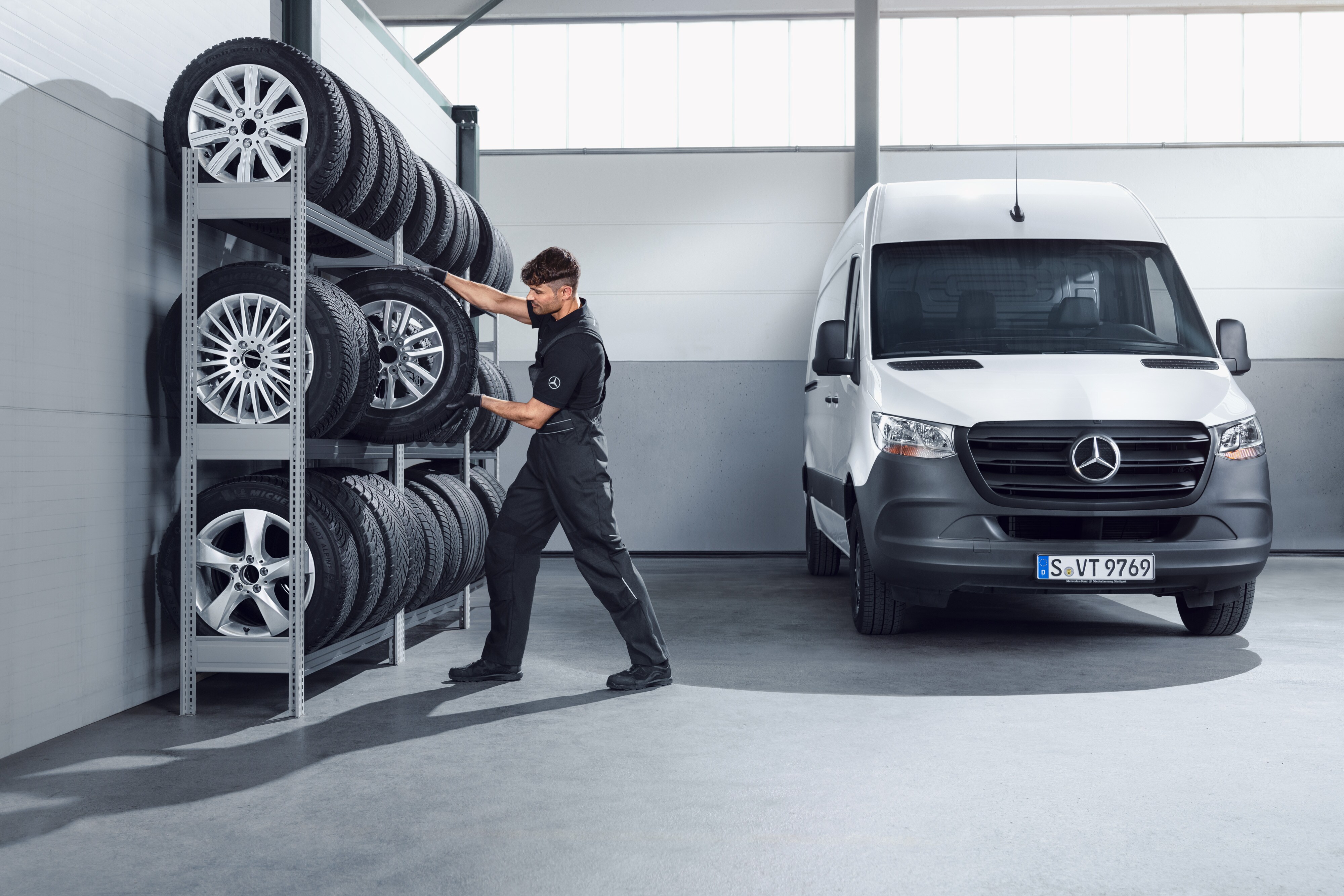 Mercedes-Benz | Transportbilar Kvalitet Originaldelar Mekaniker plockar ner Mercedes-Benz kompletta vinterhjul till en vit Sprinter från verkstadshyllan.
