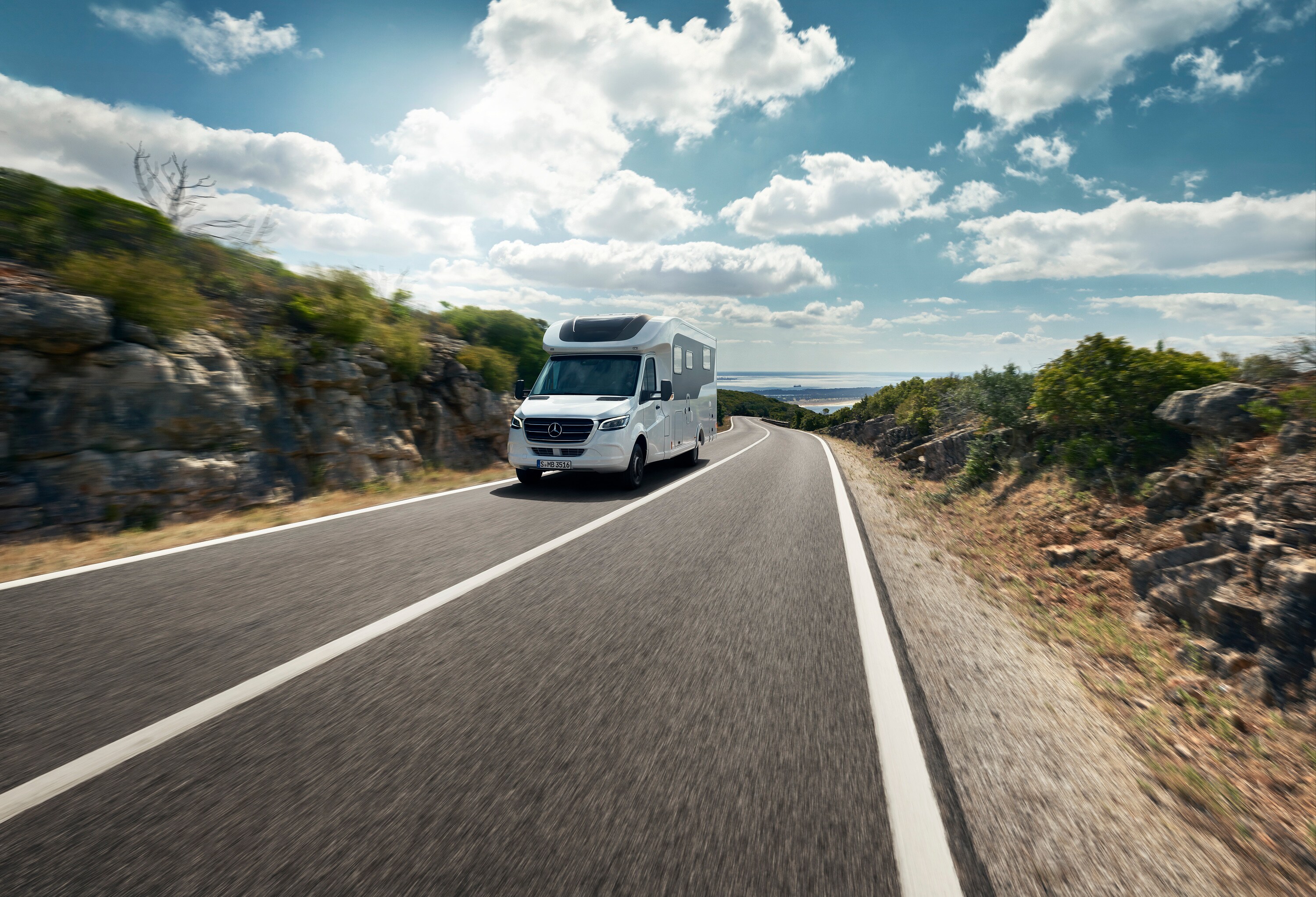 Sprinter Husbil | Campingbilar & husbilar | Mercedes-Benz Transportbilar Mercedes-Benz Sprinter husbil kör uppför bergsväg med vatten i horisonten